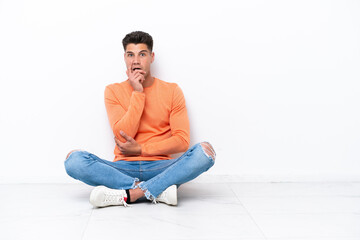 Young man sitting on the floor isolated on white background surprised and shocked while looking right