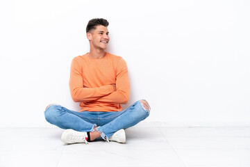 Young man sitting on the floor isolated on white background with arms crossed and happy