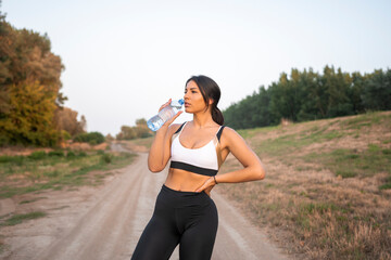 Female runner drinking water from bottle. Nature background.