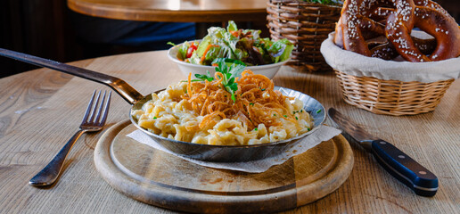 Original Käsespätzle mit Röstzwiebeln in einer eisengusspfanne auf einem Holzbrett und einem Holztisch