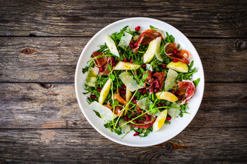 Fresh salad - prosciutto di Parma, pomegranate, pear, leafy vegetables and parmesan on wooden background
