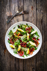 Fresh salad - prosciutto di Parma, pomegranate, pear, leafy vegetables and parmesan on wooden background
