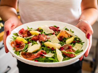 Fresh salad - prosciutto di Parma, pomegranate, pear, leafy vegetables and parmesan on wooden background
