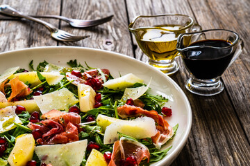Fresh salad - prosciutto di Parma, pomegranate, pear, leafy vegetables and parmesan on wooden background
