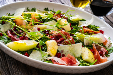 Fresh salad - prosciutto di Parma, pomegranate, pear, leafy vegetables and parmesan on wooden background
