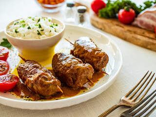 Wrapped pork served with white rice and cherry tomatoes on white table
