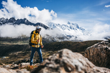 Young man outdoor traveler walk along huge sunny cloudy mountains way. Tourist with backpack and...