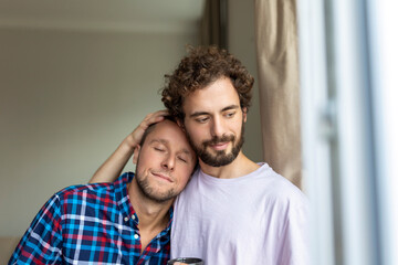 Fototapeta premium Cheerful young gay couple sitting together. Two affectionate male lovers smiling cheerfully while embracing each other. Young gay coupe being romantic.
