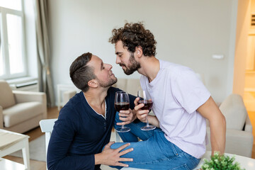 LGBTQ+ couple embracing each other and drinking wine indoors. Two romantic young male lovers looking at each other while sitting together in their living room. Young gay couple being romantic at home.