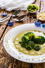 Cream broccoli soup with almonds and oregano on wooden table
