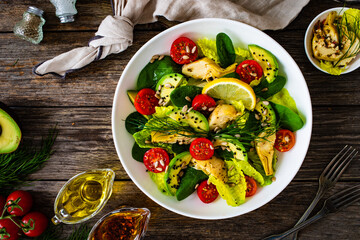 Fresh vegetable salad - avocado, artichoke, lettuce, cherry tomatoes, cucumber, arugula and spinach on wooden table 