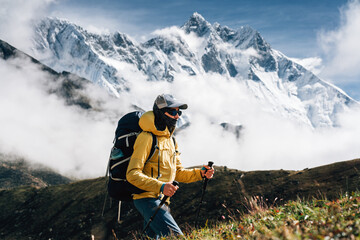 Young man outdoor traveler walk along huge sunny cloudy mountains way. Tourist with backpack and...