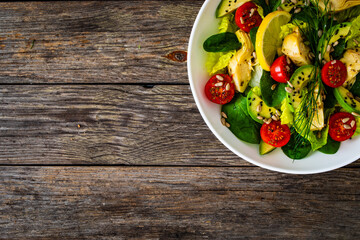 Fresh vegetable salad - avocado, artichoke, lettuce, cherry tomatoes, cucumber, arugula and spinach on wooden table 