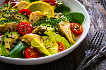 Fresh vegetable salad - avocado, artichoke, lettuce, cherry tomatoes, cucumber, arugula and spinach on wooden table 