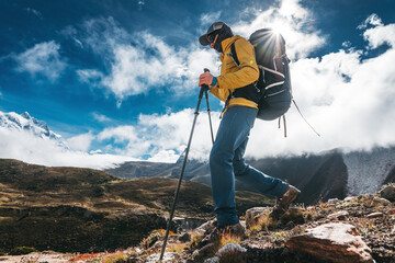 Outdoor tourist traveling along high altitude mountains wearing yellow jacket and professional backpack. Young solo hiker walk across sunny mountain track