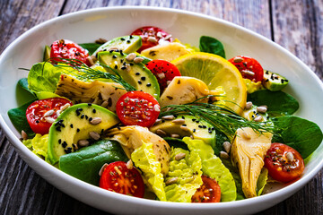 Fresh vegetable salad - avocado, artichoke, lettuce, cherry tomatoes, cucumber, arugula and spinach on wooden table 