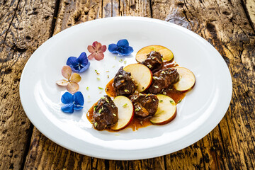 Pork cheeks in sauce with apple on wooden table