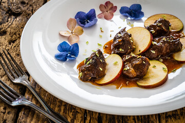 Pork cheeks in sauce with apple on wooden table