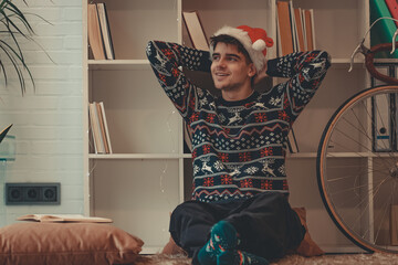 young man at home relaxed with christmas sweater and santa claus hat