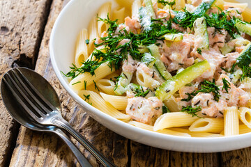 Penne with roasted salmon nuggets, dill and zucchini in cream sauce on wooden table
