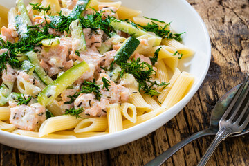 Penne with roasted salmon nuggets, dill and zucchini in cream sauce on wooden table
