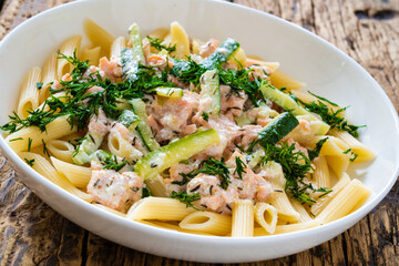 Penne with roasted salmon nuggets, dill and zucchini in cream sauce on wooden table
