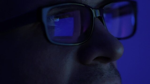 A programmer, a man in front of a computer, the code is reflected in the glasses. Working in IT, learning programming languages, developing applications and software.