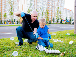 dad teaches his son to clean up the trash on the street. Volunteers. Pollution of the surrounding area. Ecology concept, plastic bottle on green grass