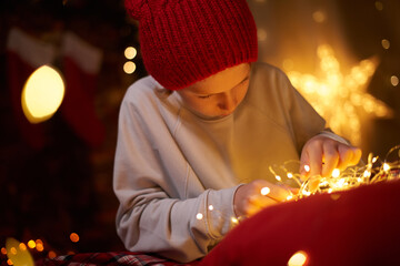 Adorable cute kid 10 years old generation Z preparing a glowing garland for Christmas at home