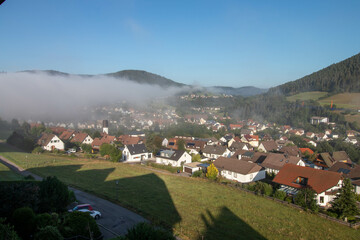 View of the Black Forest town of Baiersbronn with early morning fog in summer