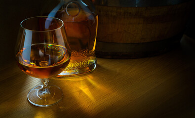 a glass of luxury alcoholic drink, an oak barrel and a bottle of cognac on a dark background; copy space