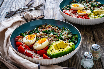 Boiled eggs with avocado, boiled red and white rice, cherry tomatoes, spinach and parmesan on wooden table
