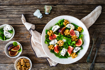 Fresh salad - goat cheese, fig, walnuts and leafy greens on wooden table
