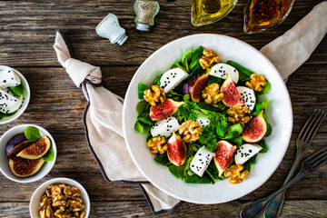 Fototapeta na wymiar Fresh salad - goat cheese, fig, walnuts and leafy greens on wooden table 