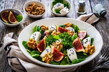 Fresh salad - goat cheese, fig, walnuts and leafy greens on wooden table
