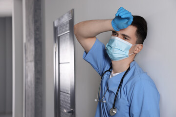 Exhausted doctor near grey wall in hospital, space for text