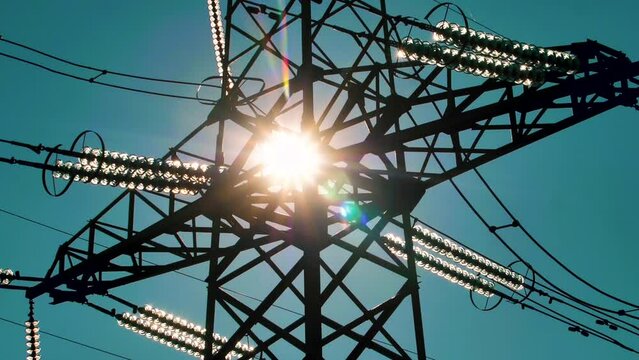 Power lines with sun rays on blue sky. High voltage substation. Electricity crisis in the world. Green energy in power lines. Selective soft focus