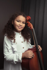 Beautiful girl in a stylish dress stands with a cello.