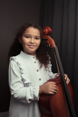 Beautiful girl in a stylish dress stands with a cello.