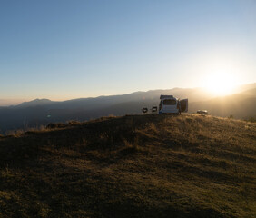 Fototapeta premium mini camper van up a hill with two chairs next to it at sunset