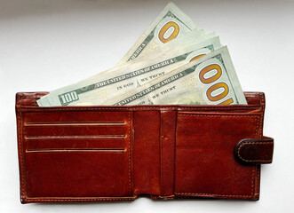 Brown leather wallet with $100 bills in close-up on a white isolated background. American currency