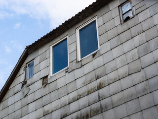 Building facade with asbestos sheets. Damaged exterior of an old house. The grey plates are fibrous material that is toxic for people and the nature. The removal of asbestos is very expensive.