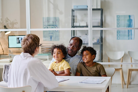 African dad with his two sons tlking to doctor while they sitting at table at hospital