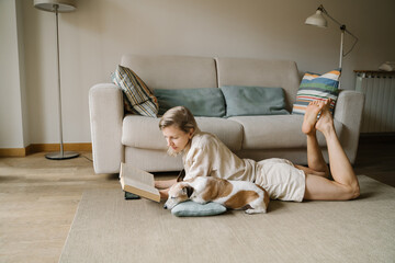 Attractive blonde woman enjoying leisure time reading novel home with small friend dog Jack Russell...