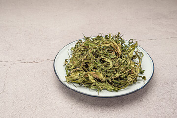 Top view of dry cannabis leaf tea on a white plate over a table