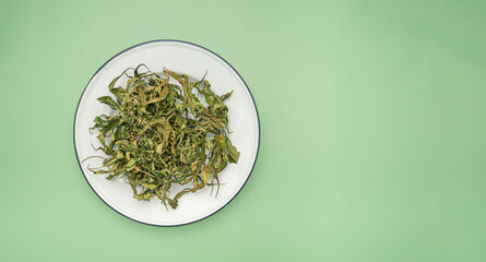 Dry cannabis leaf tea on a white plate over a green background