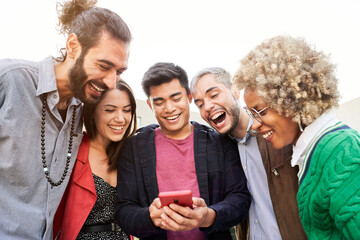 Obraz premium Group of smiling friends together using phones. Happy people watching something at mobile cell. High quality photo