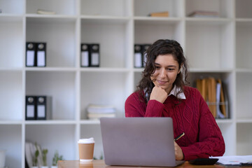 Photo of cheerful young woman working using computer laptop concentrated and smiling at office