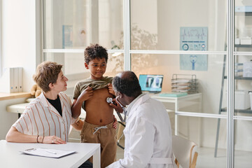 African pediatrician examining boy with stethoscope during his medical appointment
