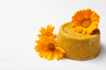 Yellow solid shampoo bar and flowers on white wooden table, closeup. Space for text